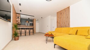 Un espace de vie moderne comprenant un canapé jaune, un coin cuisine et un ensemble de salle à manger.