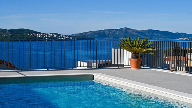 Une piscine avec vue sur la mer et les montagnes, une plante en pot et une clôture en métal.