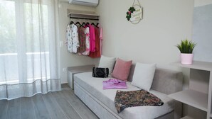 A modern room with a sofa, a hanging coat rack with clothes, a potted plant, and a wall-mounted sign. - Diana s House 2 - Gytheio Sandy Beach Haven (East Mani)