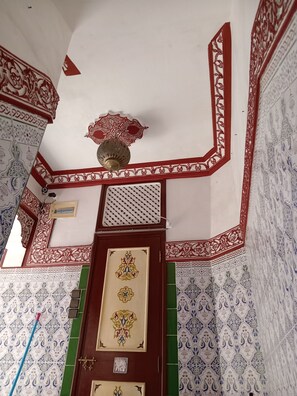 A room with ornate red and white tile patterns, a decorative ceiling fan, and a door with intricate designs. - DAR MARGOT MARRAKECH (Marrakesh)