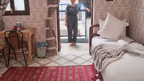 A room with a bed, a desk, a chair, a patterned rug, and a door leading outside. - DAR MARGOT MARRAKECH (Marrakesh)