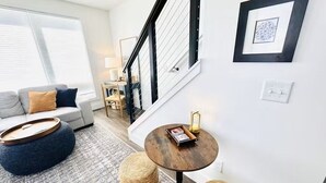 A modern living room with a sofa, ottoman, round table, and wicker stools.