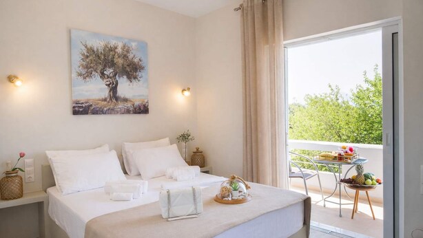 Quarto com cama, pintura, mesa com frutas e varanda com vista.