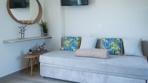 Uma sala de estar moderna com um sofá cinzento, um espelho redondo, uma TV de tela plana e uma pequena mesa lateral de madeira.