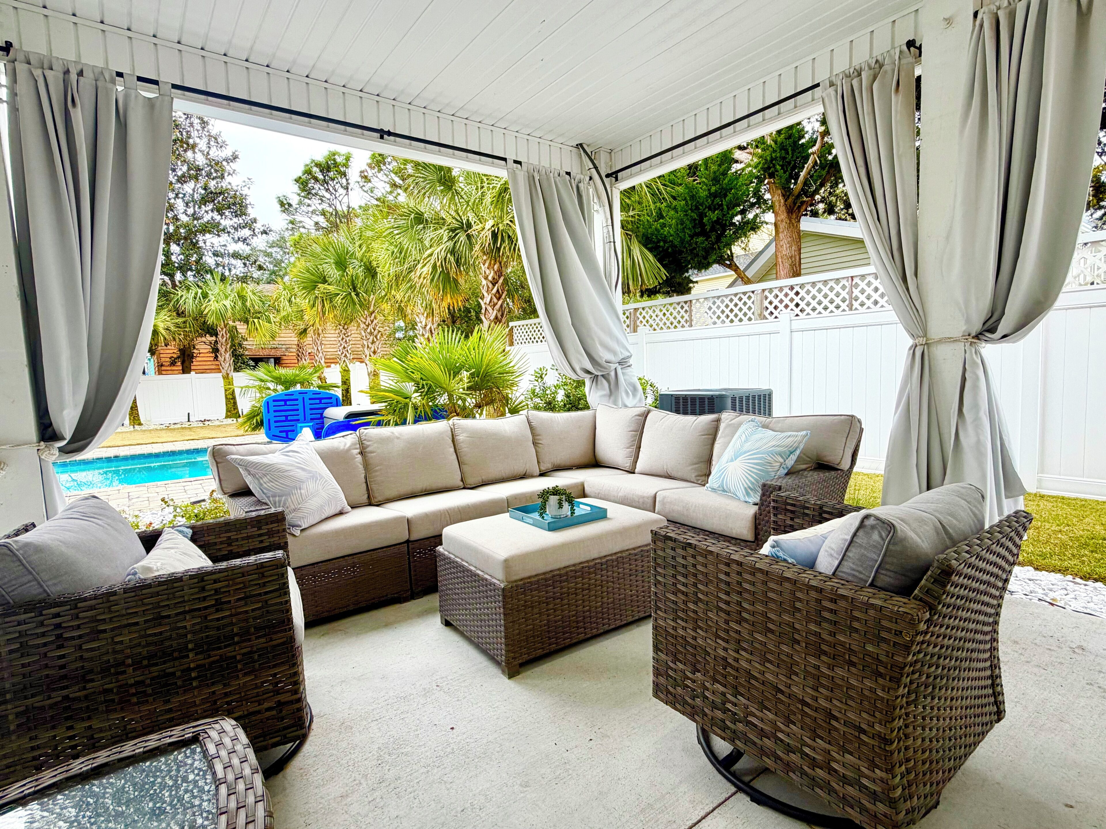 A covered outdoor seating area with a sectional sofa, wicker chairs, and a small table.