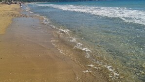 Ein Strand mit klarem Wasser, sandigem Ufer und einer entfernten Hügellandschaft.