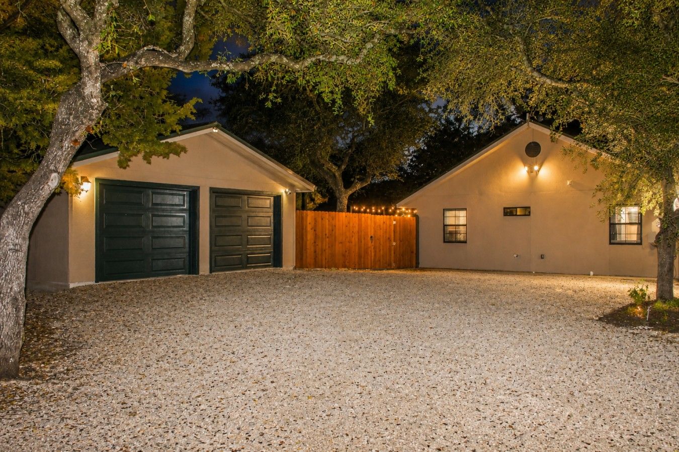 Un bâtiment à deux étages avec une allée en gravier, deux portes de garage et une clôture en bois.