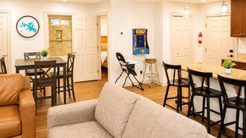 Un salon moderne avec un canapé, un coin repas avec des chaises, une cuisine avec des tabourets de bar et un jeu fixé au mur.