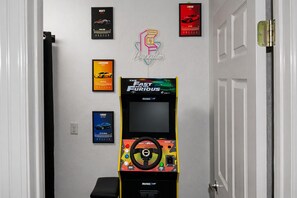 A hallway with a gaming arcade machine, framed car posters, and a neon sign. - Canyon Lake Retreat | Hot Tub + Arcade + Mini Golf | Sleeps 8 | Near Boat Ramp (Canyon Lake)