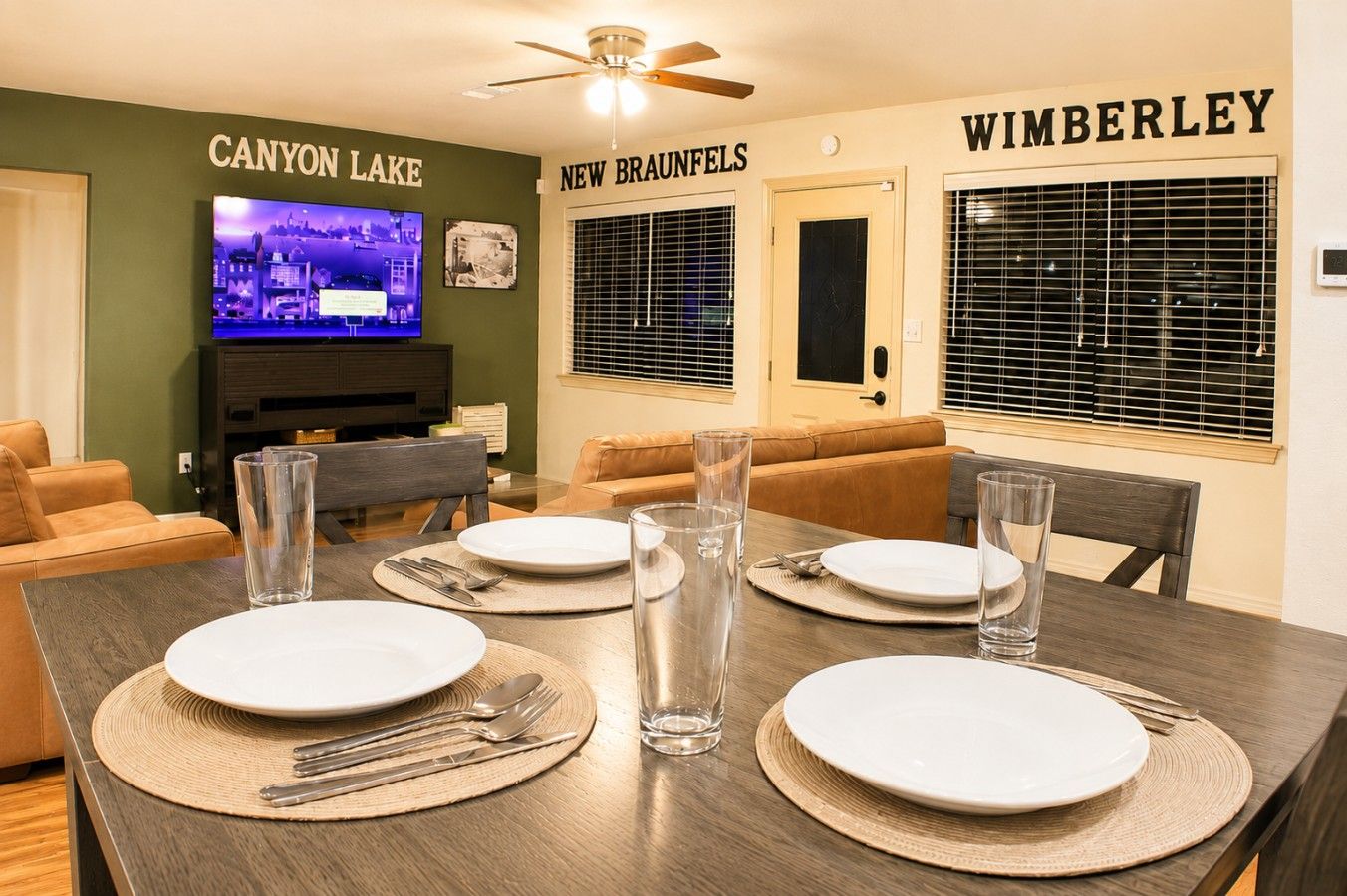 Un comedor con una mesa dispuesta para cuatro, un televisor en la pared y dos puertas con las indicaciones 'CANYON LAKE' y 'WIMBERLEY'.