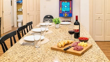 A dining table set with plates, glasses, and a bottle of wine, with a game machine in the background.