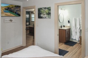 Ein Schlafzimmer mit Bett, ein Badezimmer mit Waschbecken und Handtüchern sowie ein Flur mit Kunstwerken.