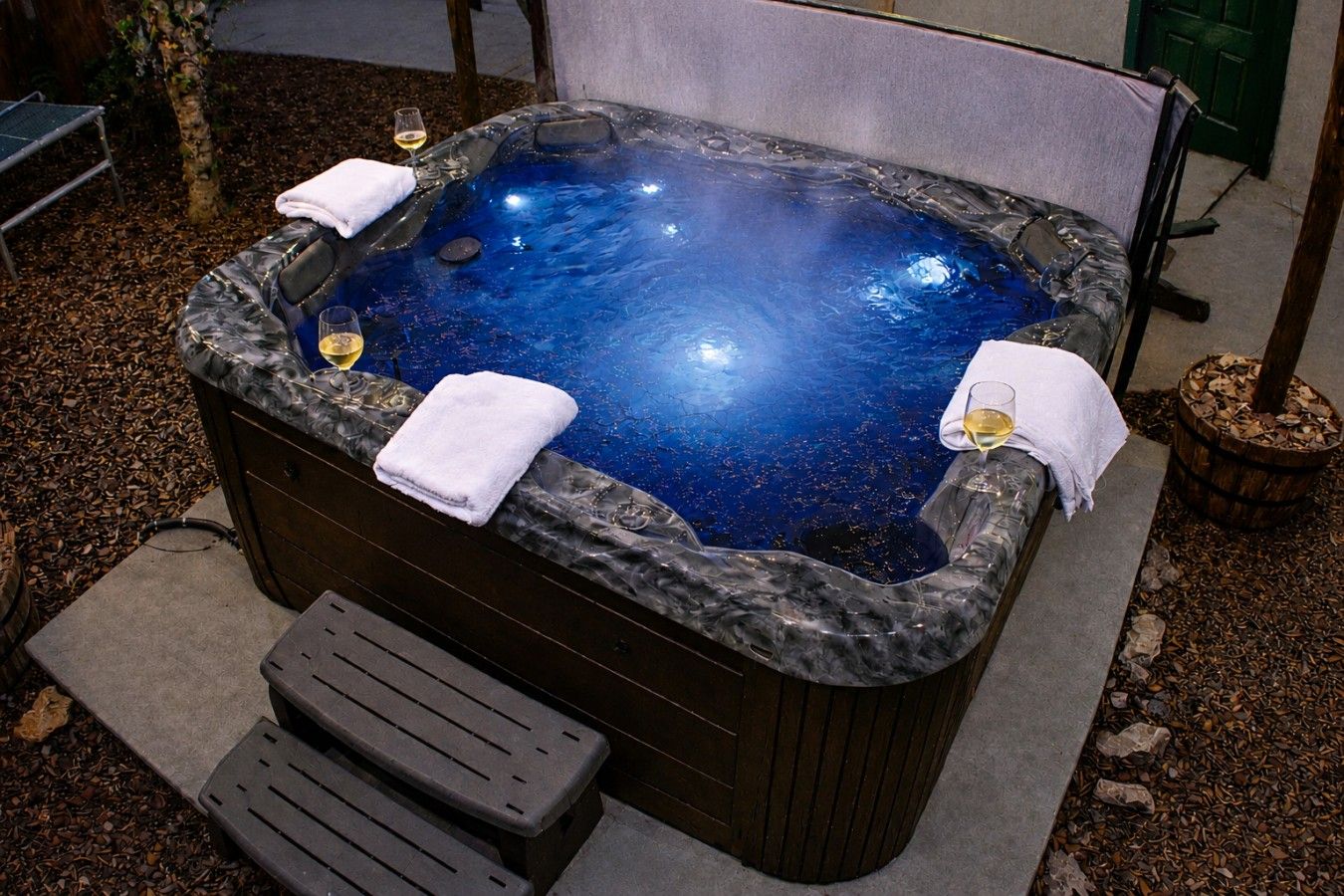 Un bain à remous avec un revêtement extérieur en marbre, deux serviettes et un verre de vin à proximité.