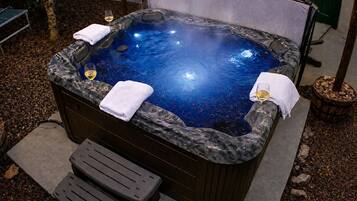 Un bain à remous avec un revêtement extérieur en marbre, deux serviettes et un verre de vin à proximité.