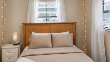 Un lit avec une tête de lit en bois, une table de chevet avec une lampe et une fenêtre avec des rideaux.