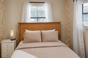 A bed with a wooden headboard, a bedside table with a lamp, and a window with curtains. - Canyon Lake Retreat | Hot Tub + Arcade + Mini Golf | Sleeps 8 | Near Boat Ramp (Canyon Lake)