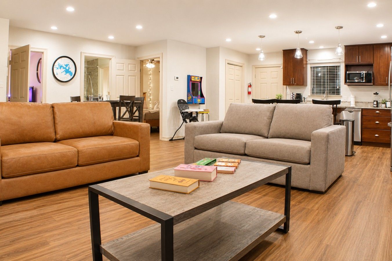 A modern living room with two sofas, a coffee table, and a kitchen area with wooden cabinets and a microwave.