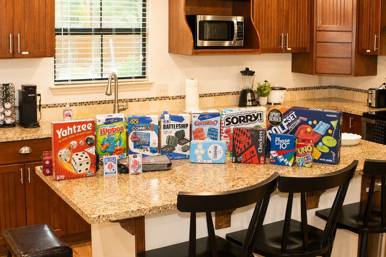 A kitchen with wooden cabinets, a microwave, and various board games on the counter.