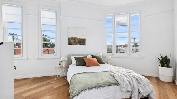 Une chambre à coucher avec un lit, un tableau, une plante et de grandes fenêtres.