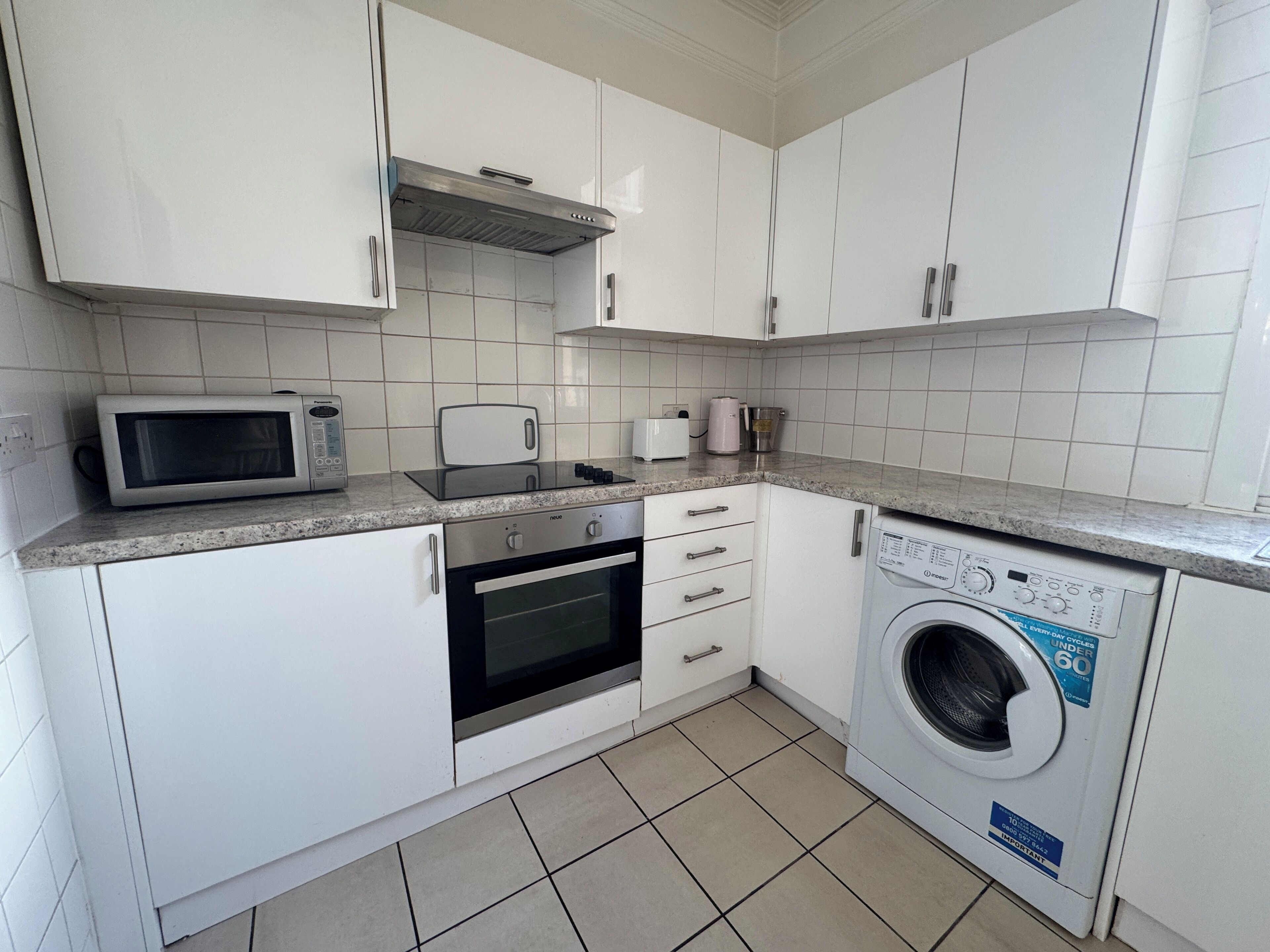 Eine Küche mit weißen Schränken, einer Mikrowelle, einem Toaster, einer Kaffeemaschine und einer Waschmaschine.