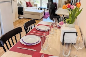 Un coin repas avec une table dressée pour quatre personnes, des chaises, un vase de tulipes et un canapé en arrière-plan.