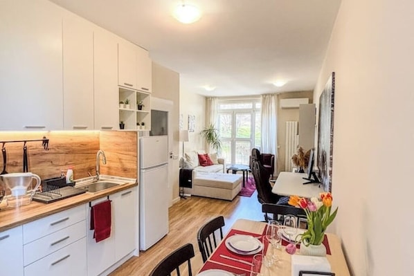 Une cuisine compacte avec des meubles blancs, un plan de travail en bois et un coin repas avec une table dressée pour deux personnes.