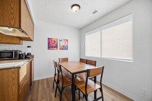 A modern kitchen with wooden cabinets, a dining table with chairs, and a window with blinds. - Central Location B in Cul de Sac, 2 Bedroom, 1 Bath-sleeps 6, pets allowed (Kennewick)