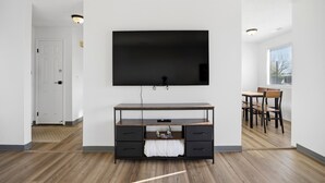 Ein modernes Wohnzimmer mit einem an der Wand befestigten Flachbildfernseher, einem Holztisch und einem Essbereich mit Stühlen.