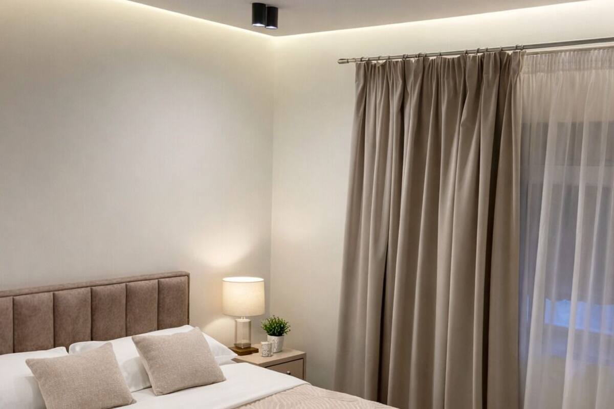 Un dormitorio moderno con una cama grande, una mesita de noche con lámpara y una ventana con cortinas.