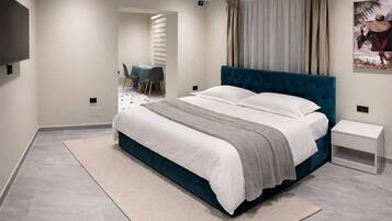 A modern bedroom with a large bed, a bedside table, a wall-mounted air conditioner, and a view of a dining area.