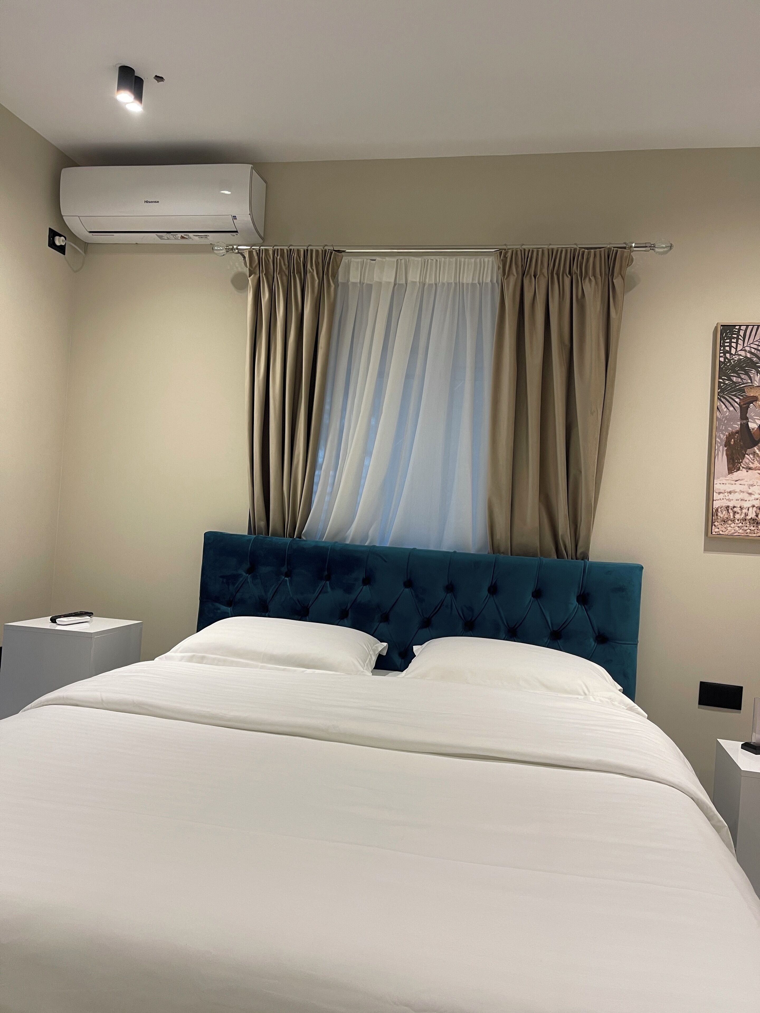 Een hotelkamer met een bed, nachtkastje, airconditioning en een raam met gordijnen.