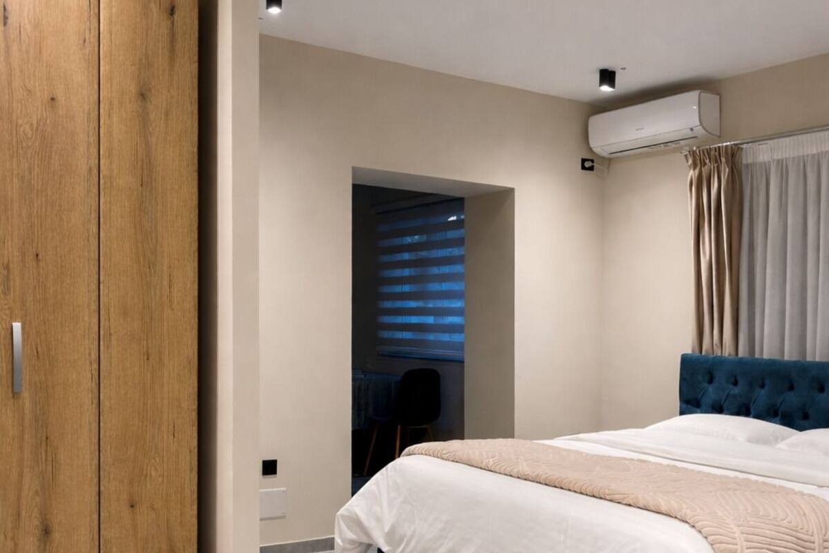 Un dormitorio con cama, armario, ventana con cortinas y aire acondicionado.