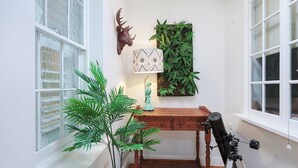 Habitació d'angle amb escriptori de fusta, un telescopi, un cervós decoratiu, una làmpada amb dibuixos i una planta penjant de color verd.