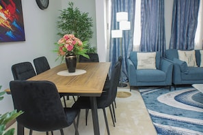 Un salon moderne avec une table à manger en bois, des chaises noires, un canapé bleu orné de coussins à motifs et un tapis bleu à motifs.