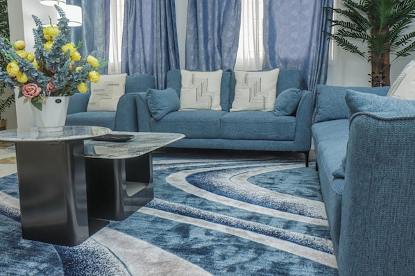 Un salon avec un canapé bleu, des coussins à motifs, une table basse ronde et un tapis bleu et blanc.