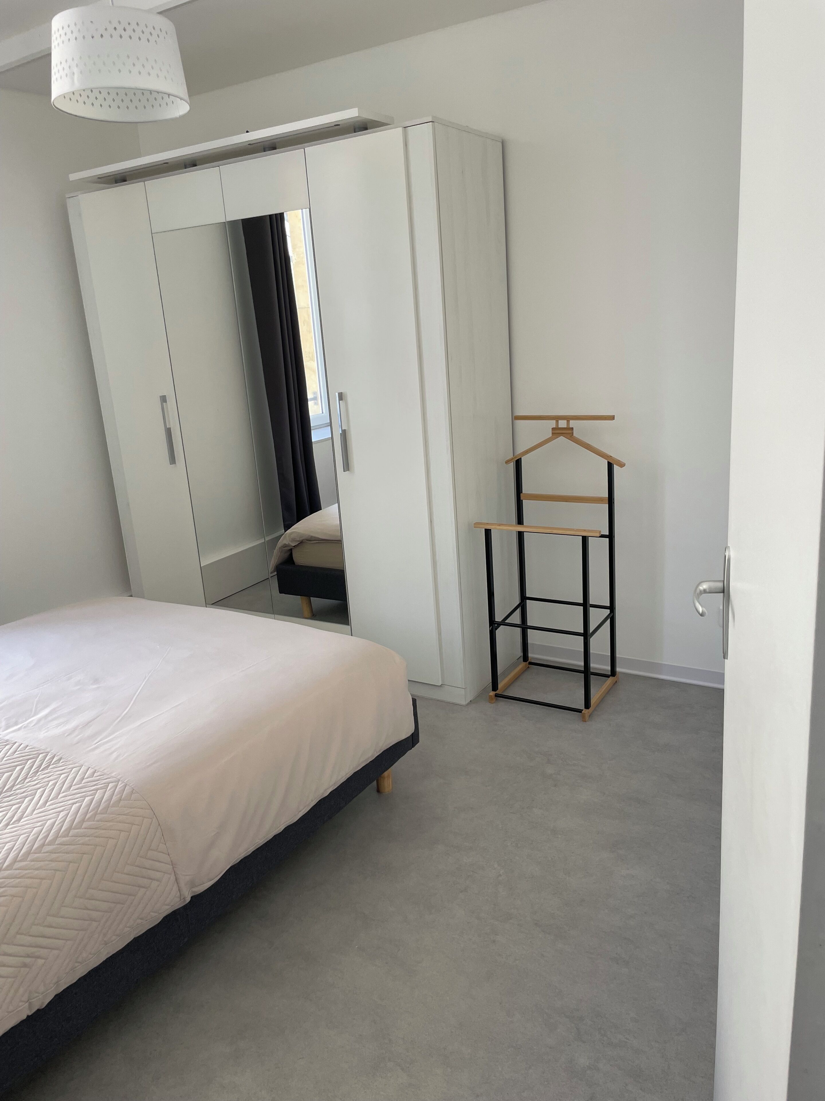 A bedroom with a bed, a wardrobe, a mirror, and a clothing rack.