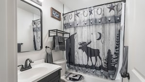 A bathroom with a white sink, a mirror, a toilet, and a shower curtain with a moose and stars design.