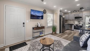 A modern kitchen with stainless steel appliances, a dining area with a gray sofa, and a ceiling fan.