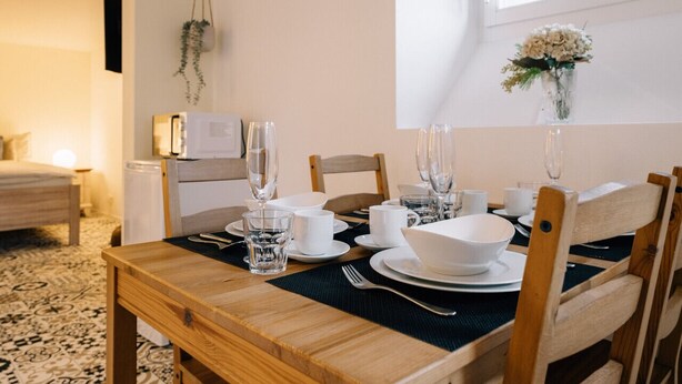 Un coin repas avec une table en bois mise pour quatre personnes, comprenant des assiettes, des tasses et des verres blancs.