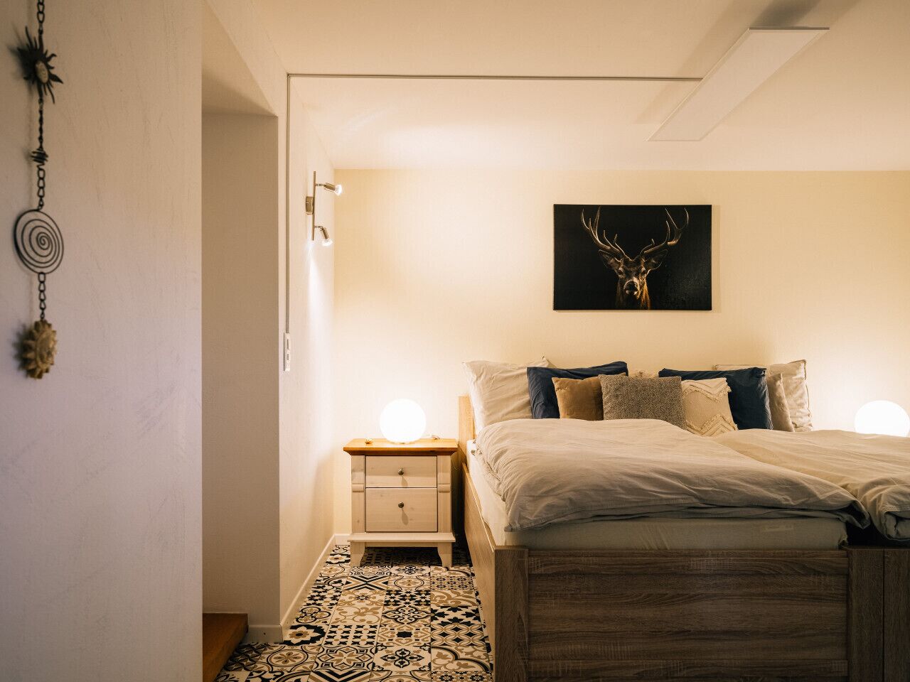 A bedroom with a bed, bedside lamps, a wall-mounted artwork, and a patterned rug.