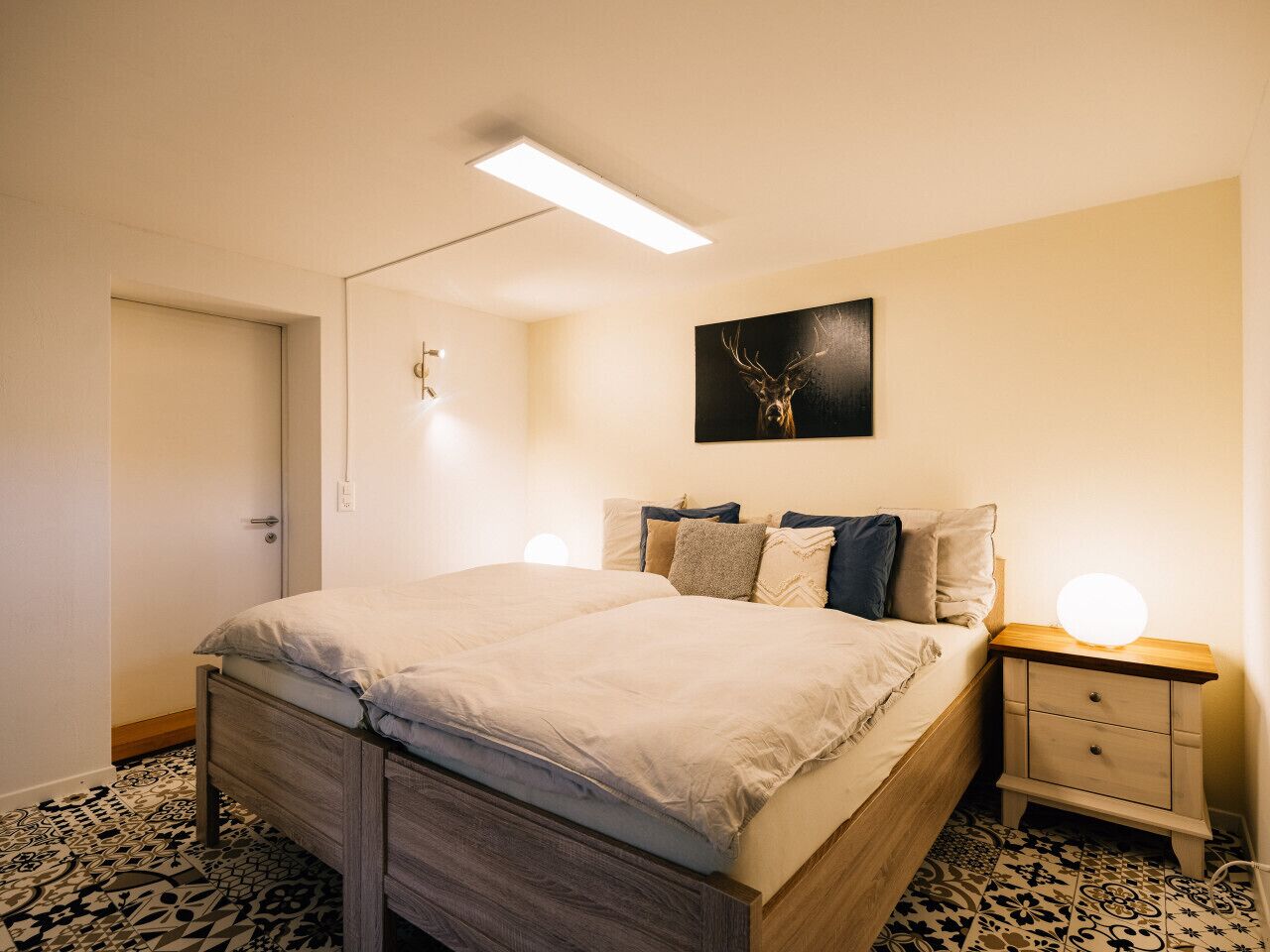 Une chambre à coucher avec un lit, des tables de chevet, une lampe fixée au mur et une porte.