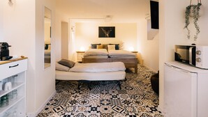 Une chambre à coucher avec un lit, des tables de chevet, un miroir, une plante suspendue et un four à micro-ondes posé sur une petite étagère.