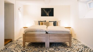 Une chambre à coucher avec un lit placé au centre, sous une œuvre d’art accrochée au mur, un sol à motifs et une petite table de chevet avec une lampe.