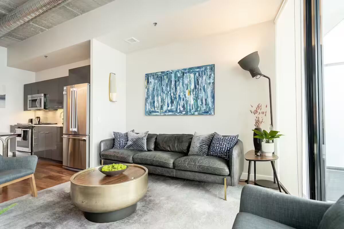 A modern living room with a grey sofa, a round coffee table, and a large abstract painting on the wall.