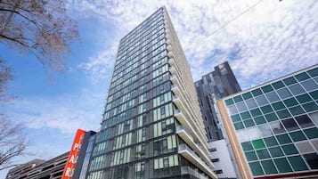 A modern high-rise building with a glass facade, surrounded by other buildings and a clear sky.