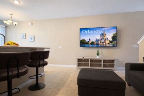 Een moderne woonkamer met een flatscreen-tv waarop een stadsbeeld wordt getoond, een barruimte met krukken en een gezellige zithoek.