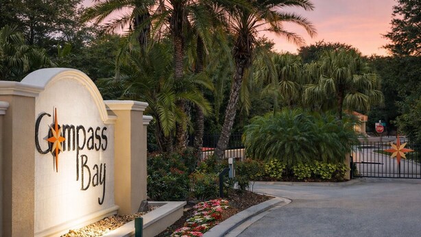Señal de Compass Bay con una entrada ajardinada que presenta palmeras y plantas con flores.