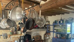 Een landelijke keuken met hangende pannen, een fornuis, een spoelbak en een eethoek met een tafel en stoelen.