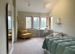 A bedroom with a bed, a desk, and a chair. There are windows and a mirror on the wall.