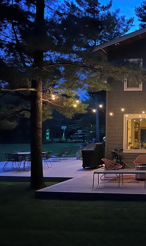 A patio area with outdoor seating and a grill, overlooking a body of water and trees.